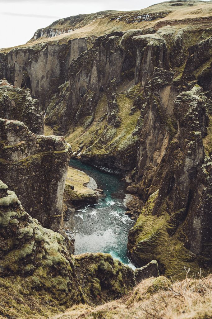 Blick von oben in den Fjaðrárgljúfur Canyon in Island mit steilen Felswänden und blauem Fluss zwischen moosigen Hängen