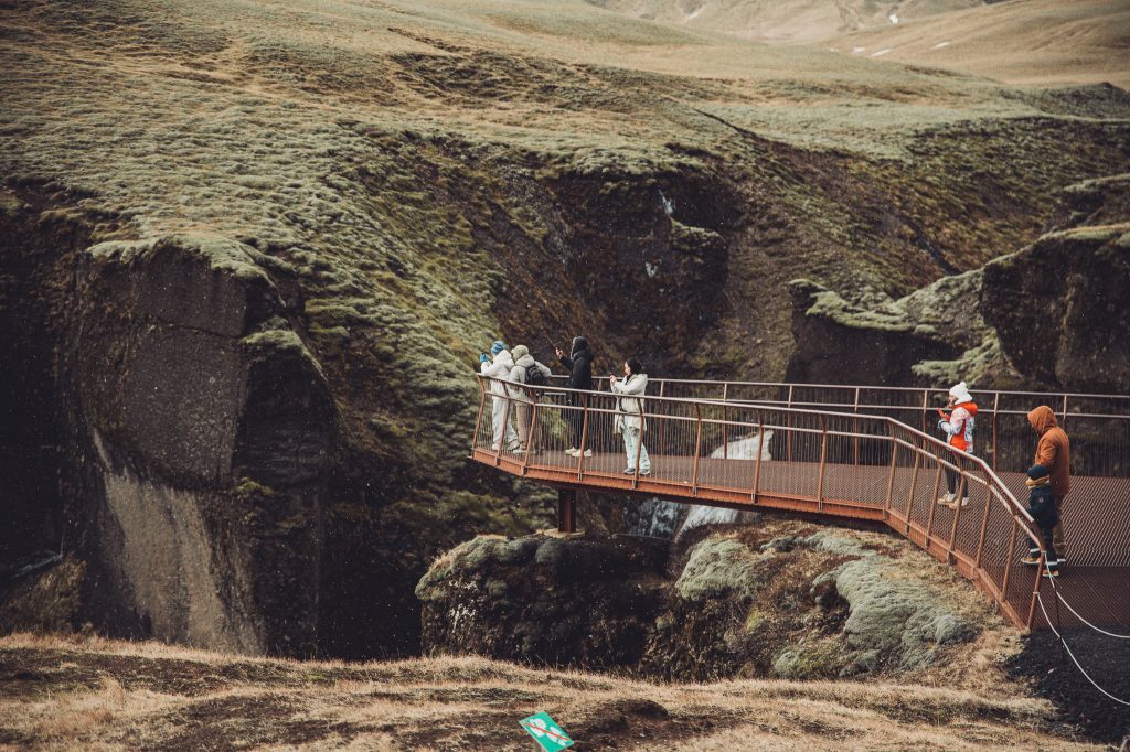 Aussichtsplattform mit Besucherinnen und Besuchern am Fjaðrárgljúfur Canyon in Island vor moosigen Felswänden