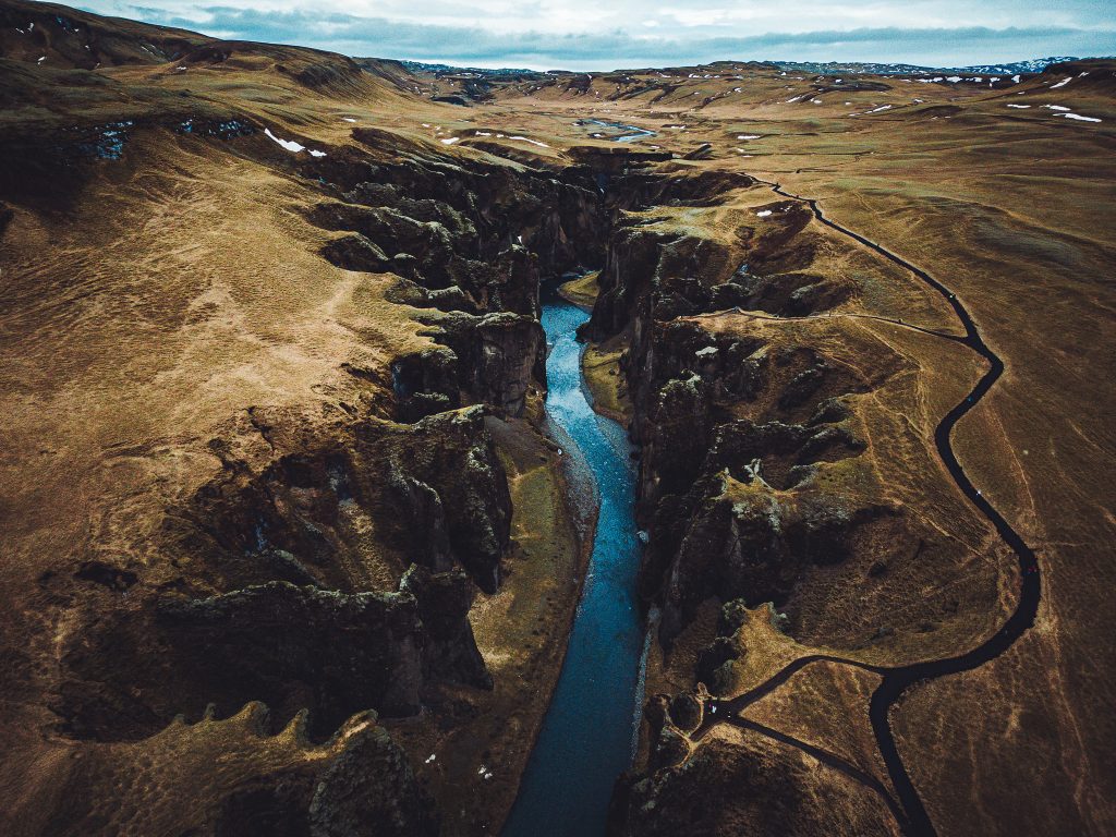 Große Drohnenaufnahme des Fjaðrárgljúfur Canyon in Island mit Fluss, weiten Hängen und schwarzem Wanderweg am Rand