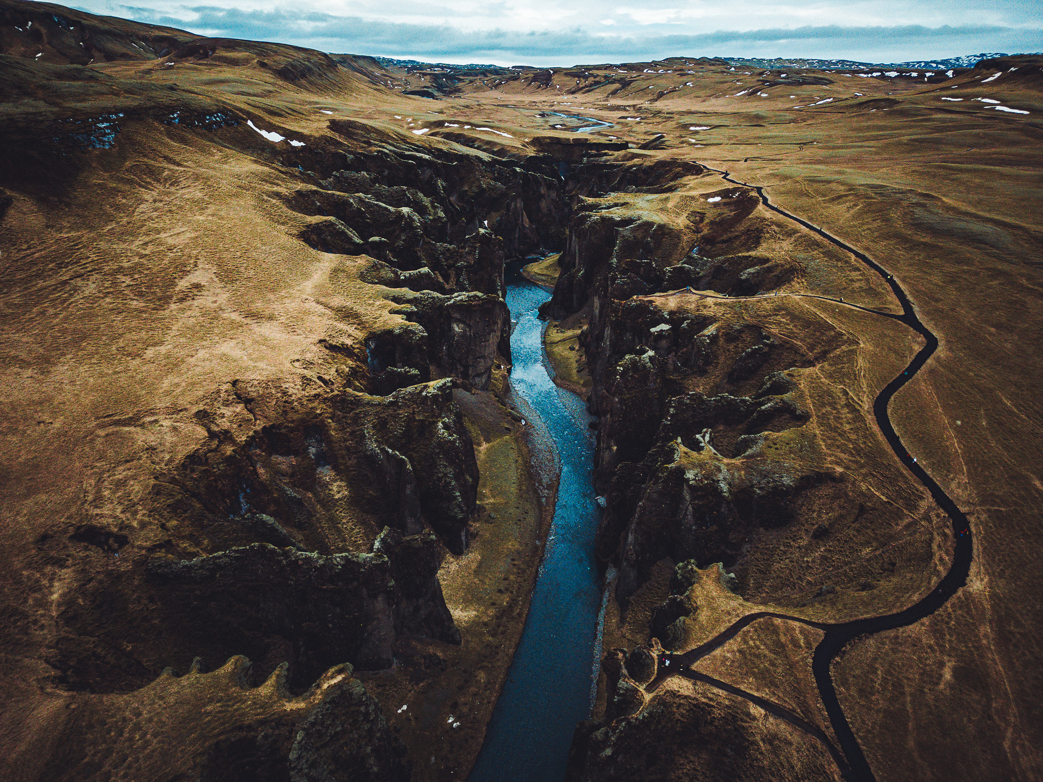 Große Drohnenaufnahme des Fjaðrárgljúfur Canyon in Island mit Fluss, weiten Hängen und schwarzem Wanderweg am Rand