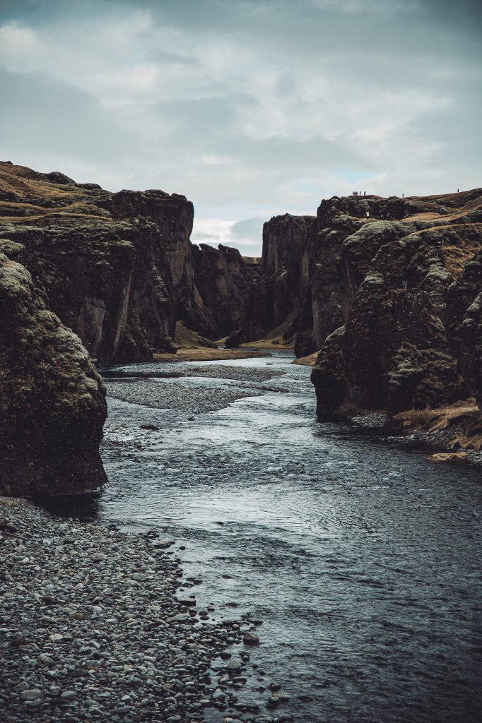 Fjaðrárgljúfur Canyon in Island mit Fluss, Kiesufer und hohen dunklen Felswänden unter bewölktem Himmel