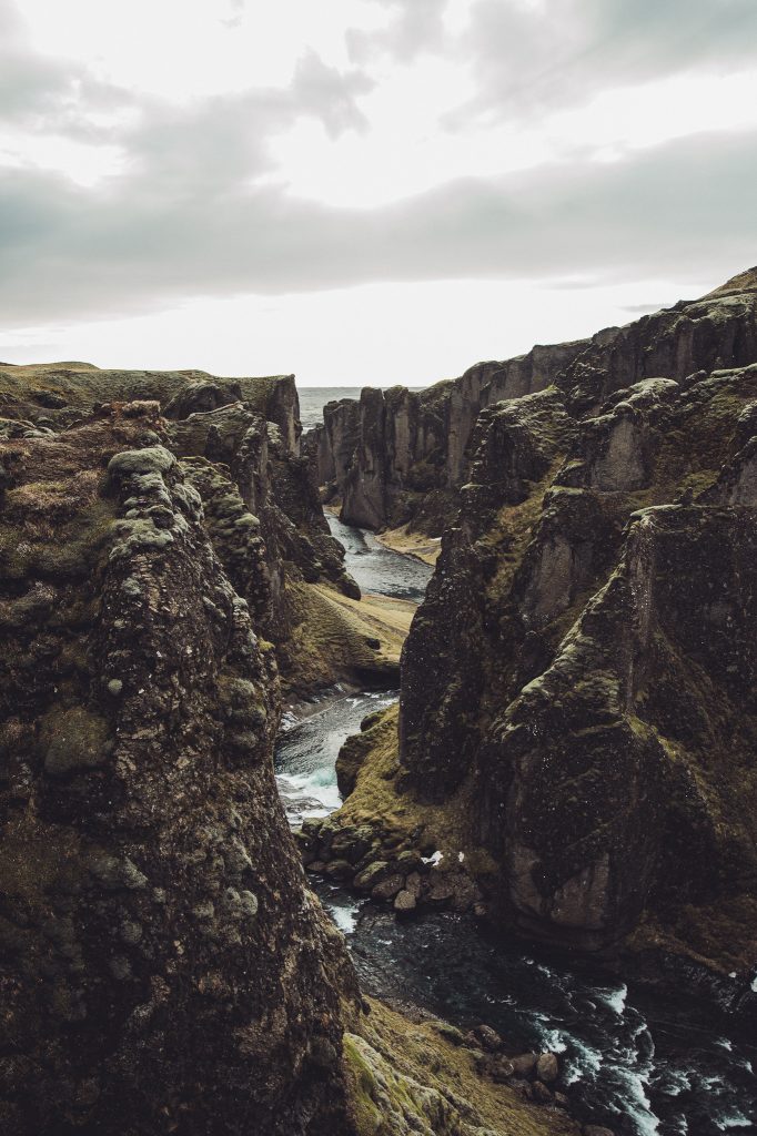 Panoramablick auf den Fjaðrárgljúfur Canyon in Island mit hohen Felsformationen, Fluss und dramatischem Himmel