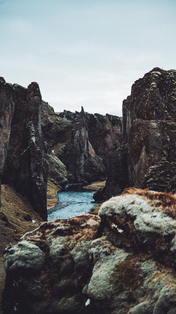 Enge Passage im Fjaðrárgljúfur Canyon mit dunklen Felsen, moosigem Vordergrund und blauem Fluss in Island