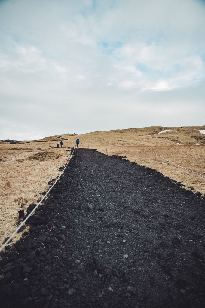 Schwarzer Wanderweg aus Vulkangestein am Fjaðrárgljúfur Canyon in Island mit offenem Grasland und wenigen Menschen