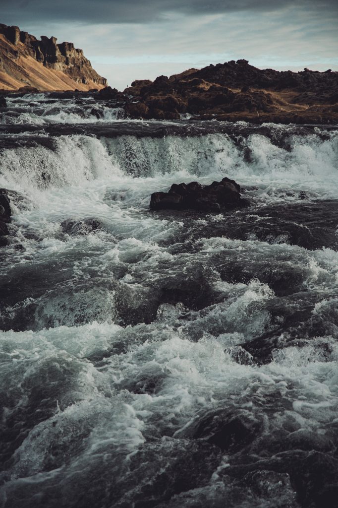 Fossálar Wasserfall in Island mit breiter Kaskade, schäumendem Wasser, dunklen Lavasteinen und Felsen im Hintergrund