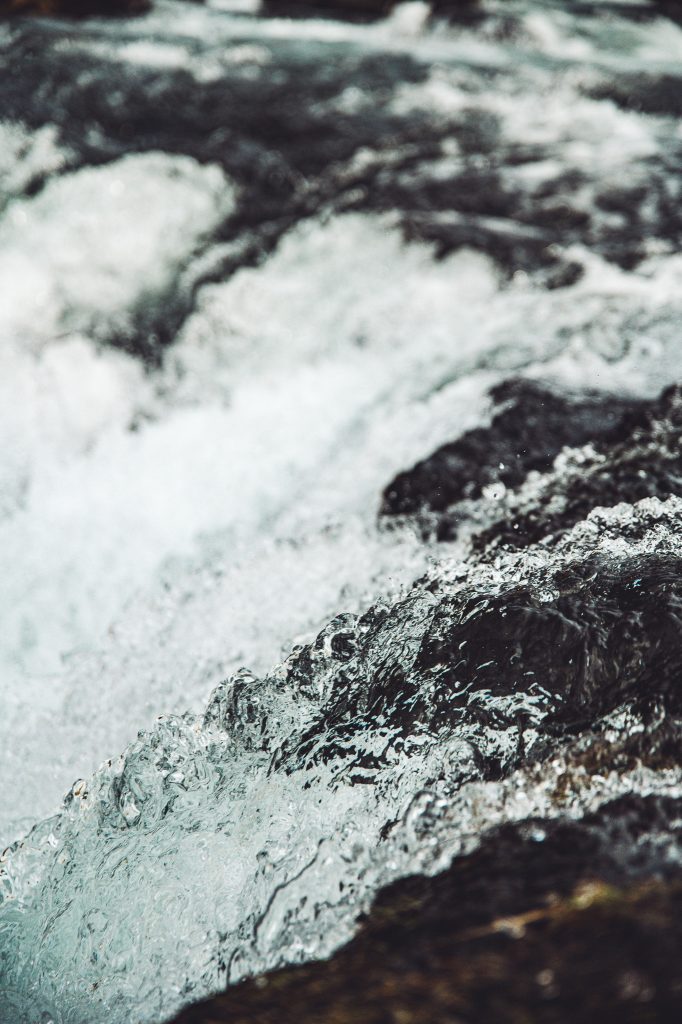 Detailaufnahme von Wasser und Gischt am Fossálar Wasserfall in Island mit klarer Strömung über dunklem Lavagestein