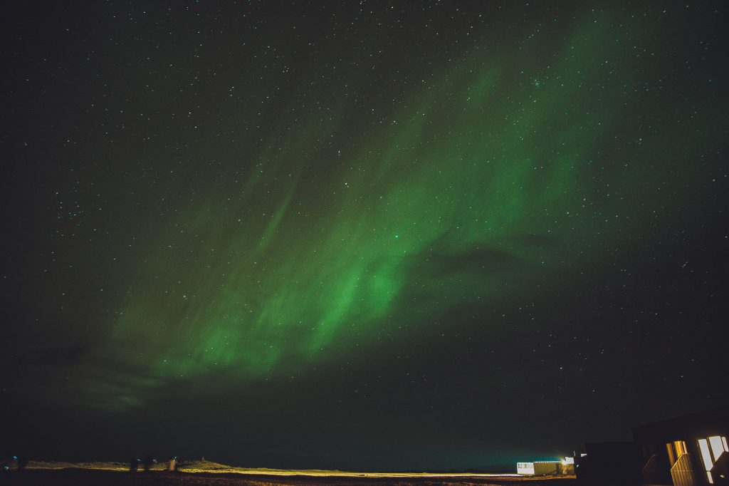 Schwache grüne Polarlichter über sternenklarem Himmel und dunkler Landschaft nahe dem Fosshotel Núpar in Südisland