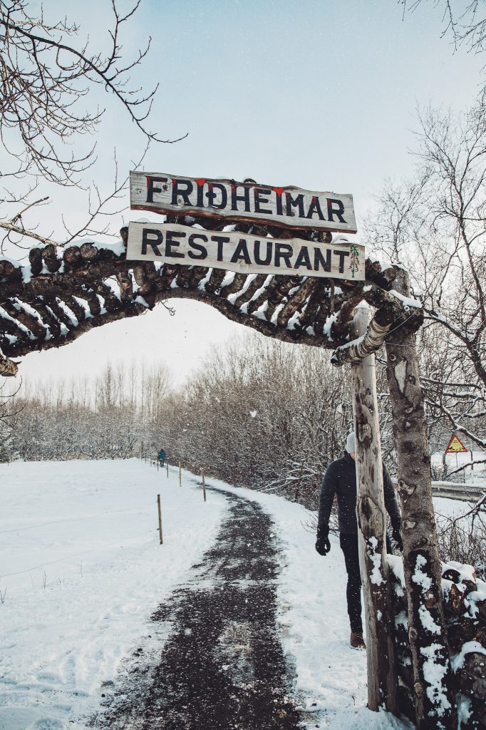 Verschneiter Weg unter dem Holztor mit Friðheimar-Restaurant-Schild bei Flúðir in Island