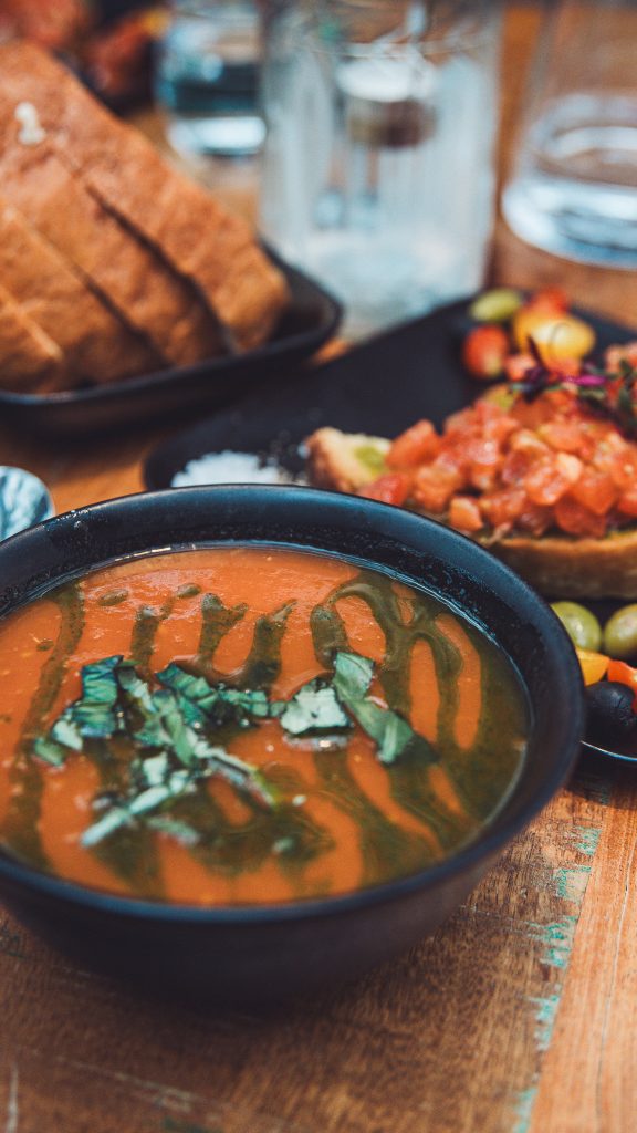Schale mit Tomatensuppe und Brot auf einem Holztisch im Bistro von Friðheimar
