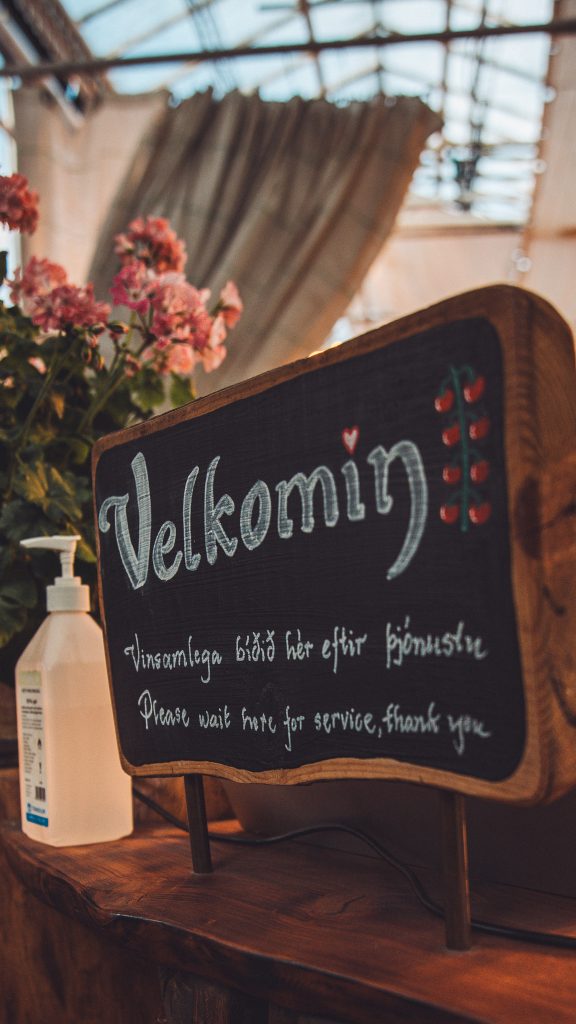 Willkommensschild im Gewächshaus von Friðheimar mit Blumen und Holztresen