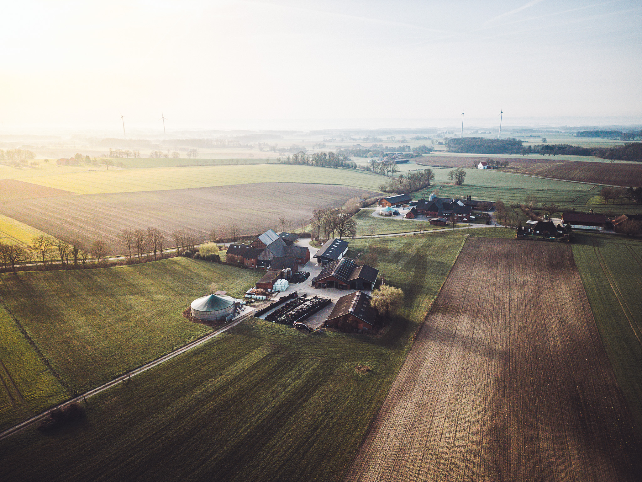 Drohnenaufnahme vom Hof Becker vor der Sandfort mit Hofgebäuden, Feldern und weiter Landschaft rund um den Stellplatz