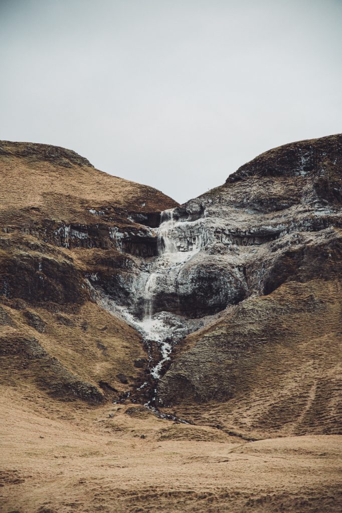 Kleiner Wasserfall in einer braunen Hanglandschaft auf der Route nach Flúðir in Island