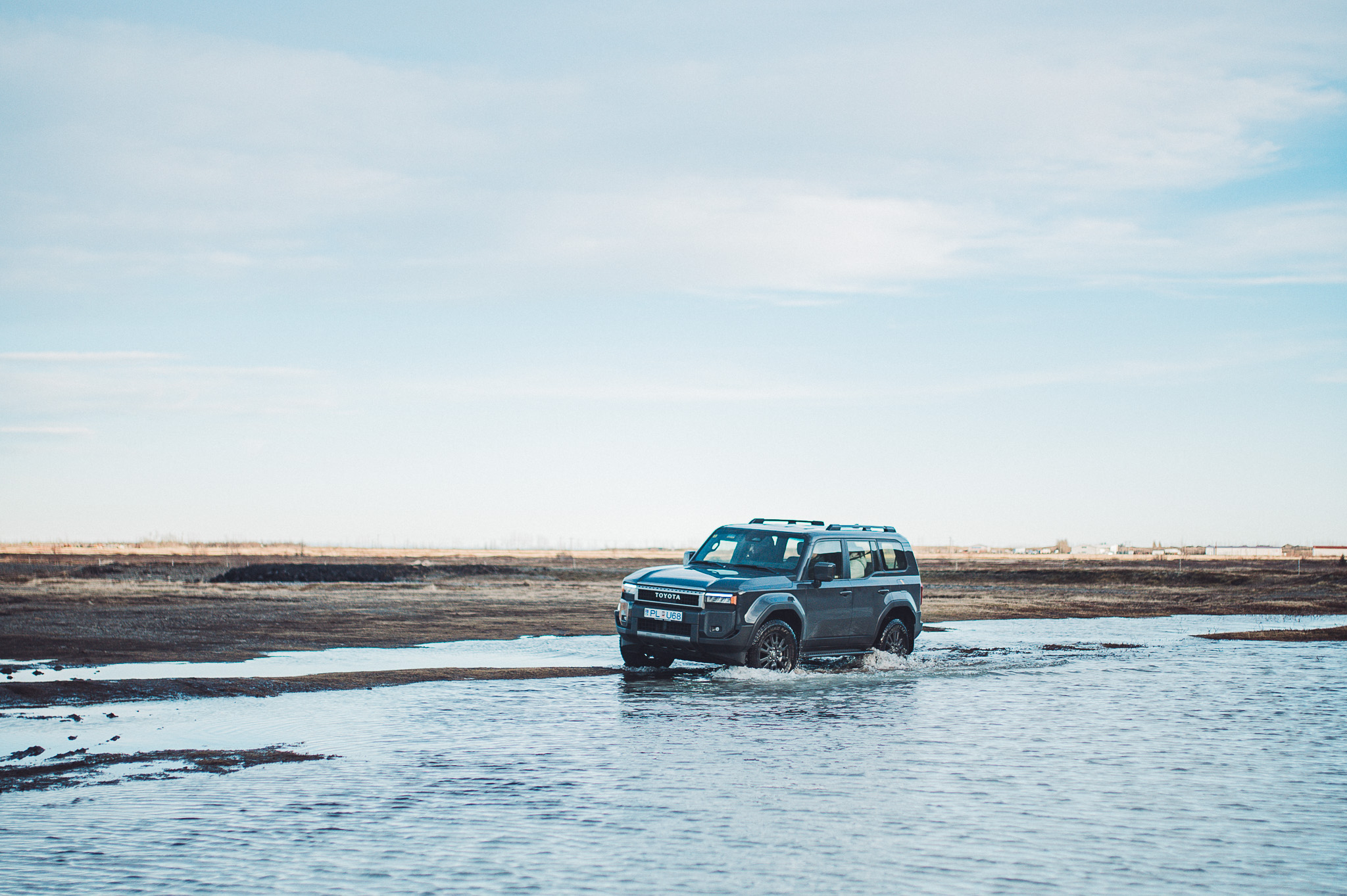 Grauer SUV fährt durch flaches Wasser auf schwarzem Untergrund nahe dem Stjórnarfoss in Südisland