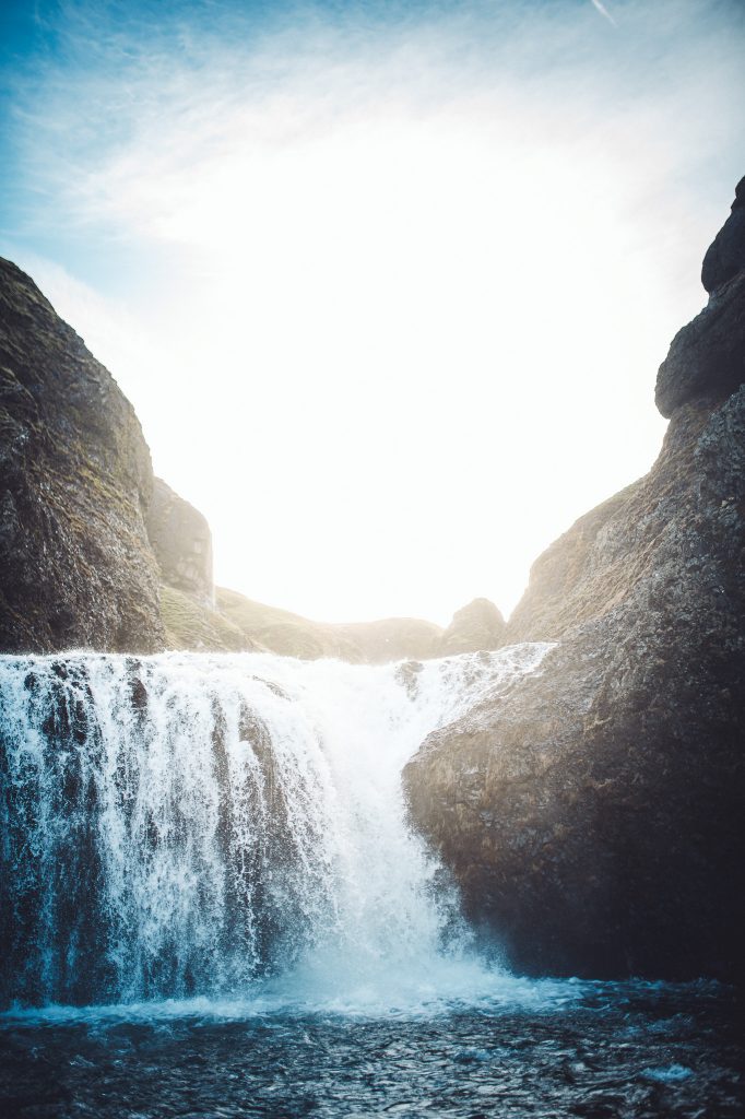 Vertikales Foto vom Stjórnarfoss Wasserfall in Südisland mit hellem Himmel, dunklen Felswänden und weißem Wasser