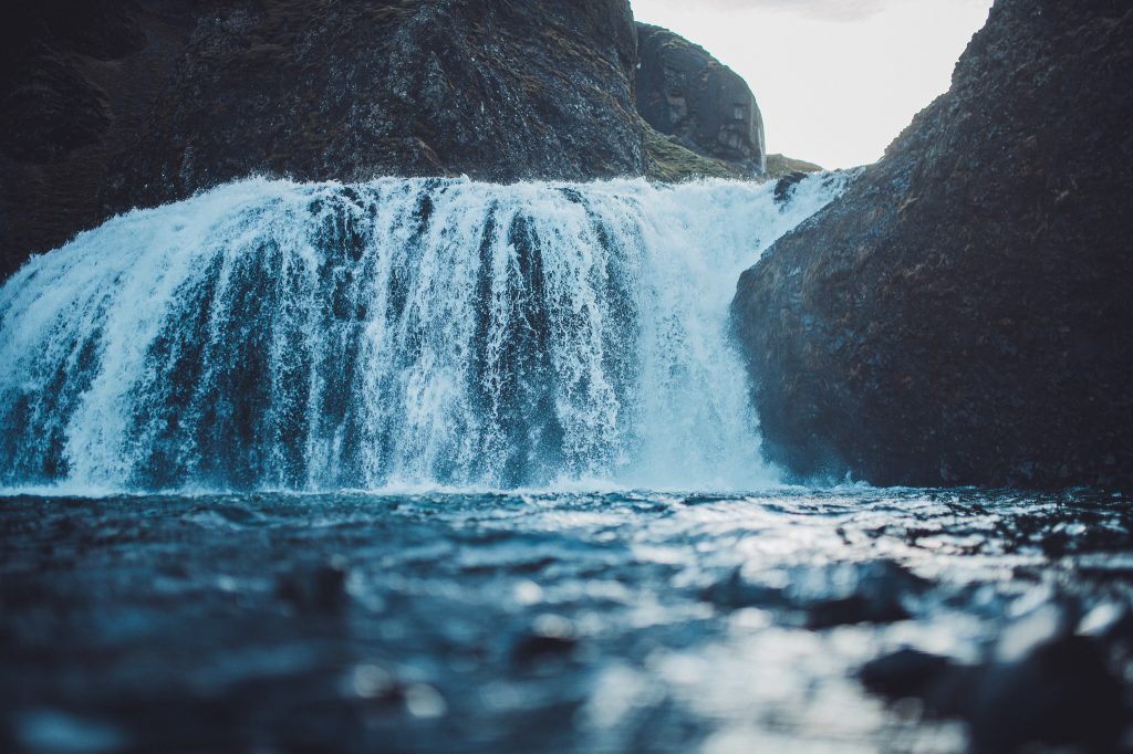Nahaufnahme des Stjórnarfoss in Südisland mit breiter Wasserfallkante, dunklen Felsen und fließendem Wasser im Vordergrund