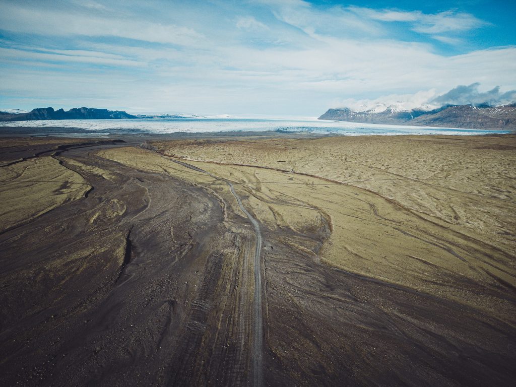 Drohnenaufnahme einer weiten Gletscherlandschaft in Südisland mit Straße, dunklem Sand und Eis im Hintergrund
