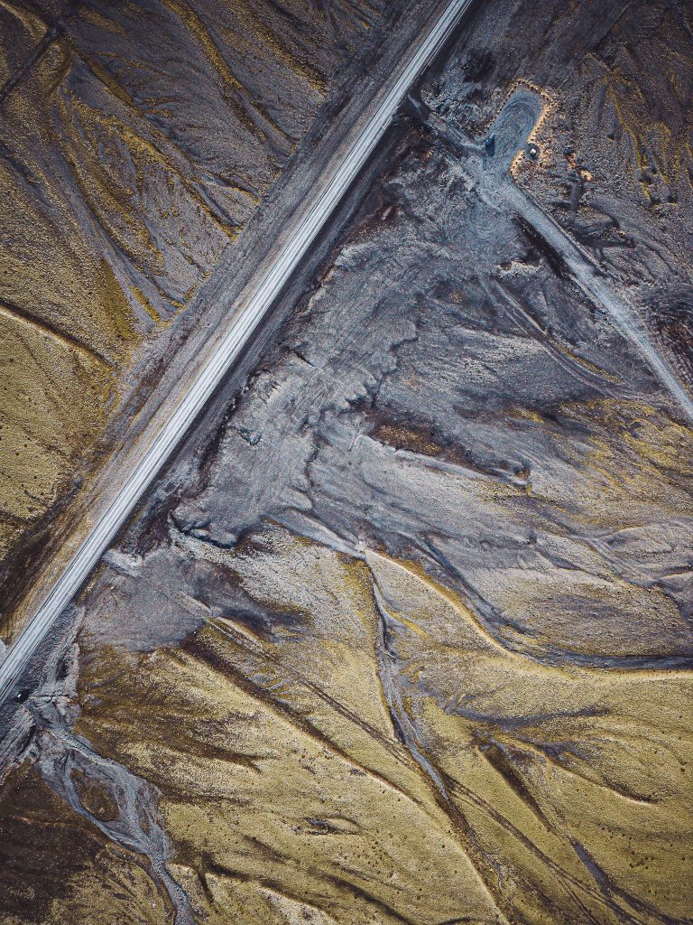 Top-down-Drohnenfoto einer Straße durch graue und gelbliche Sandflächen in Südisland