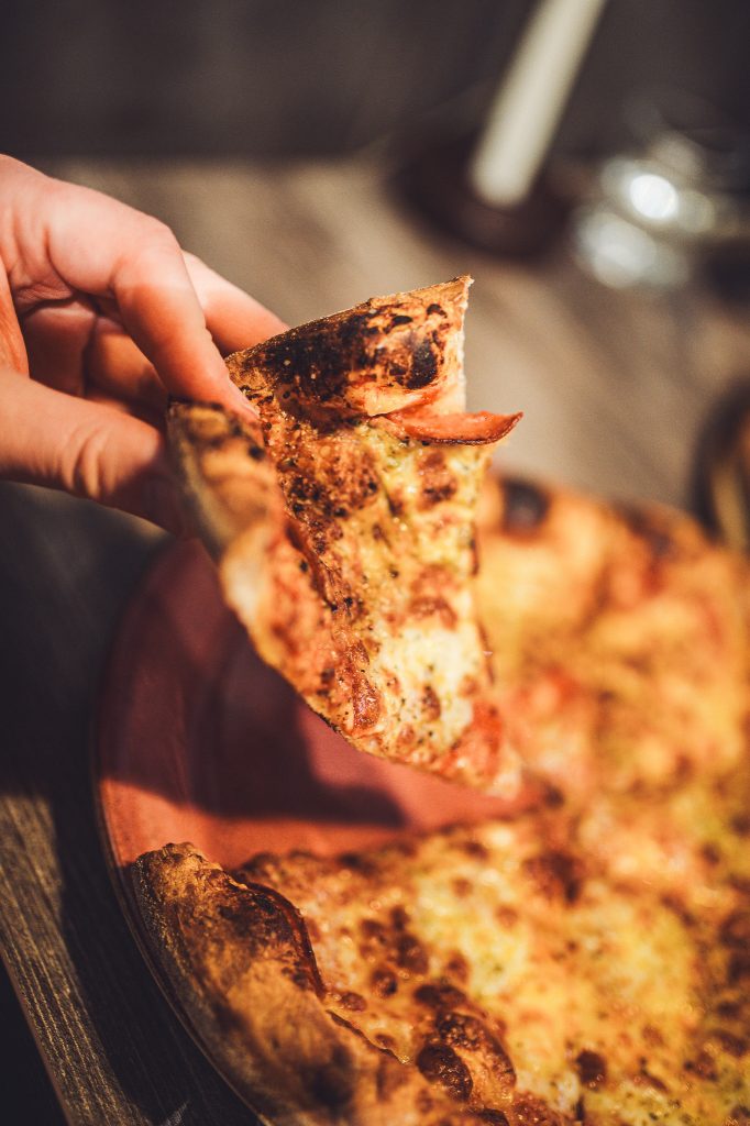 Hand hält ein Stück Pizza über einem Teller im Systrakaffi Restaurant in Südisland