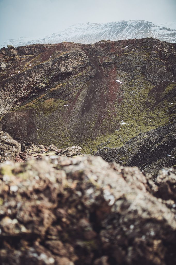 Steiler Innenhang des Eldborg-Kraters in Island mit Schneegipfeln im Hintergrund