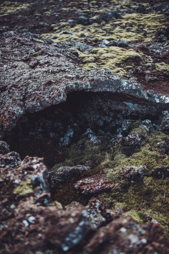 Rugged lava rock formation with a dark hollow crevice and mossy surface.