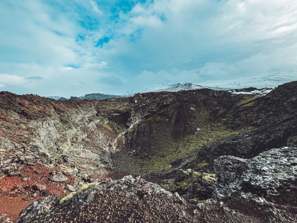 Weiter Blick in den Eldborg-Krater in Island mit felsigen Hängen und Wolkenhimmel