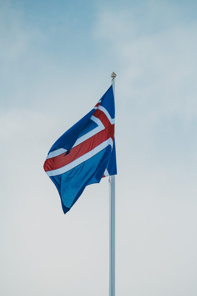 Isländische Flagge an einem Fahnenmast vor grauem Winterhimmel in Island