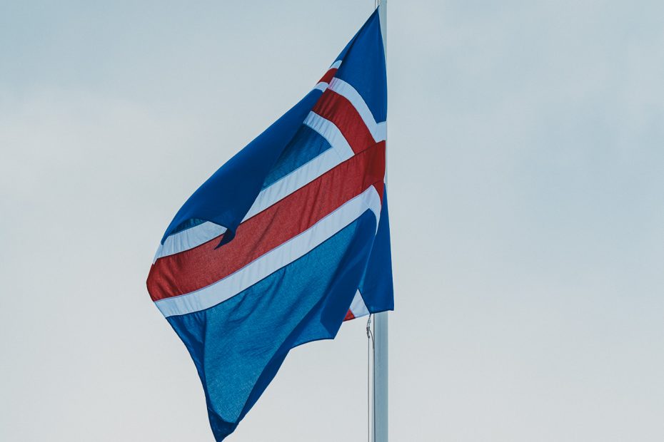 Isländische Flagge an einem Fahnenmast vor grauem Winterhimmel in Island