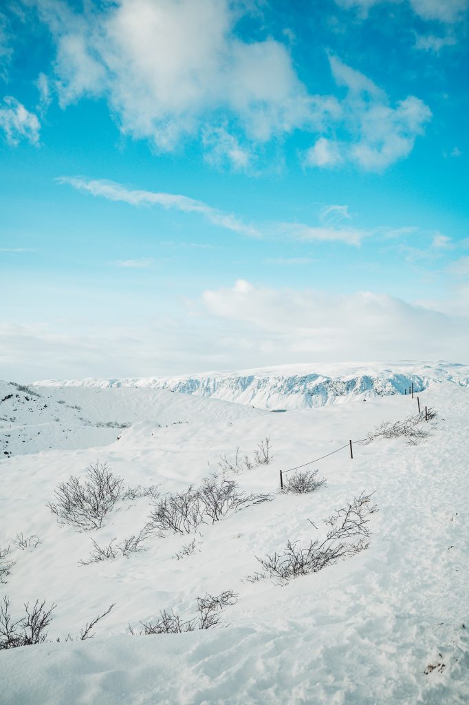 Verschneiter Weg am Kerið-Krater in Island mit weiter Winterlandschaft, blauem Himmel und vereistem Gelände