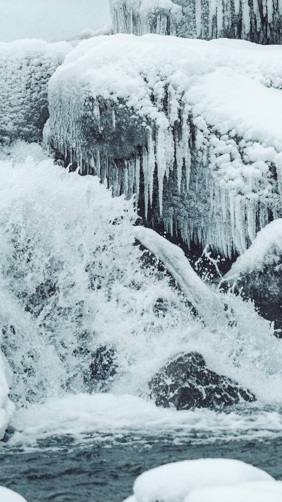 Nahaufnahme von Eiszapfen, Schnee und fließendem Wasser am Öxarárfoss im Winter in Island