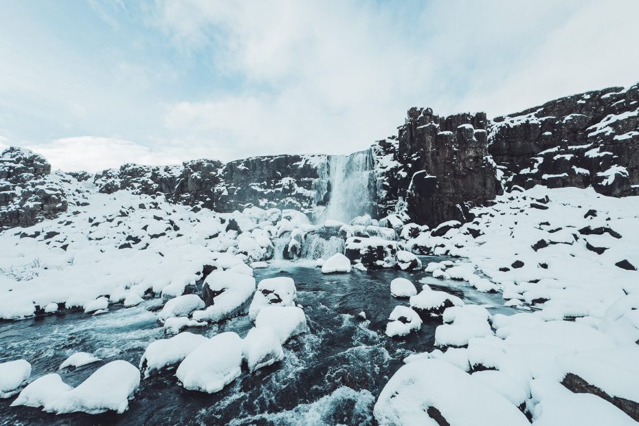 Breiter Blick auf den Öxarárfoss mit verschneiten Felsen und fließendem Wasser im winterlichen Þingvellir-Nationalpark