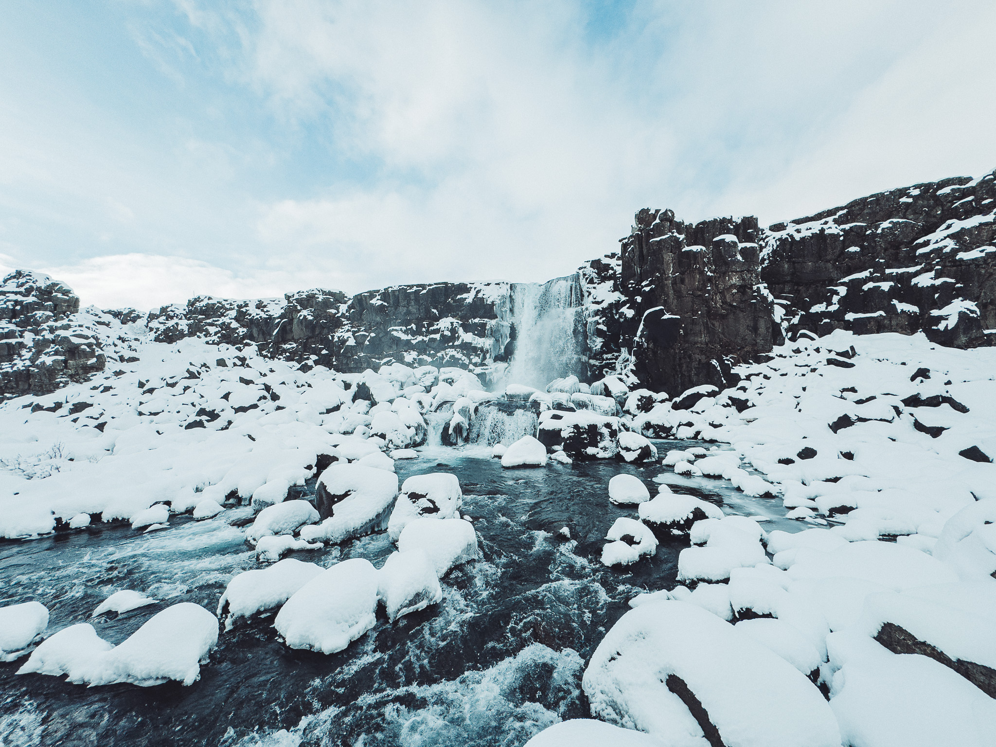Breiter Blick auf den Öxarárfoss mit verschneiten Felsen und fließendem Wasser im winterlichen Þingvellir-Nationalpark