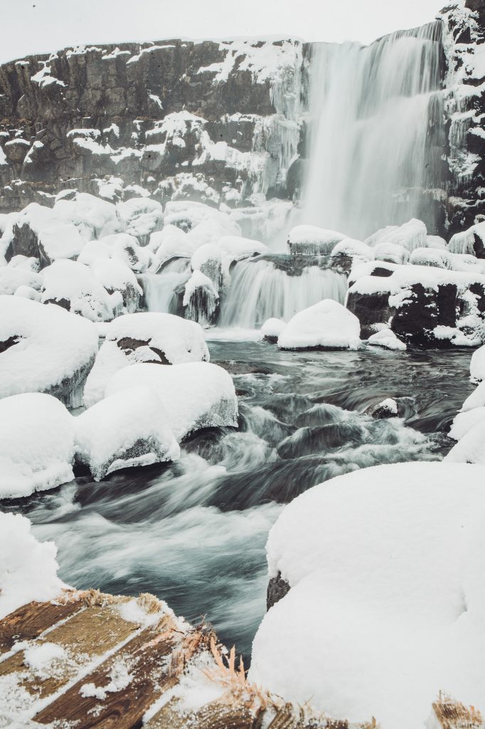 Winterlicher Blick auf den Öxarárfoss mit Schnee auf den Felsen und fließendem Wasser im Þingvellir-Nationalpark