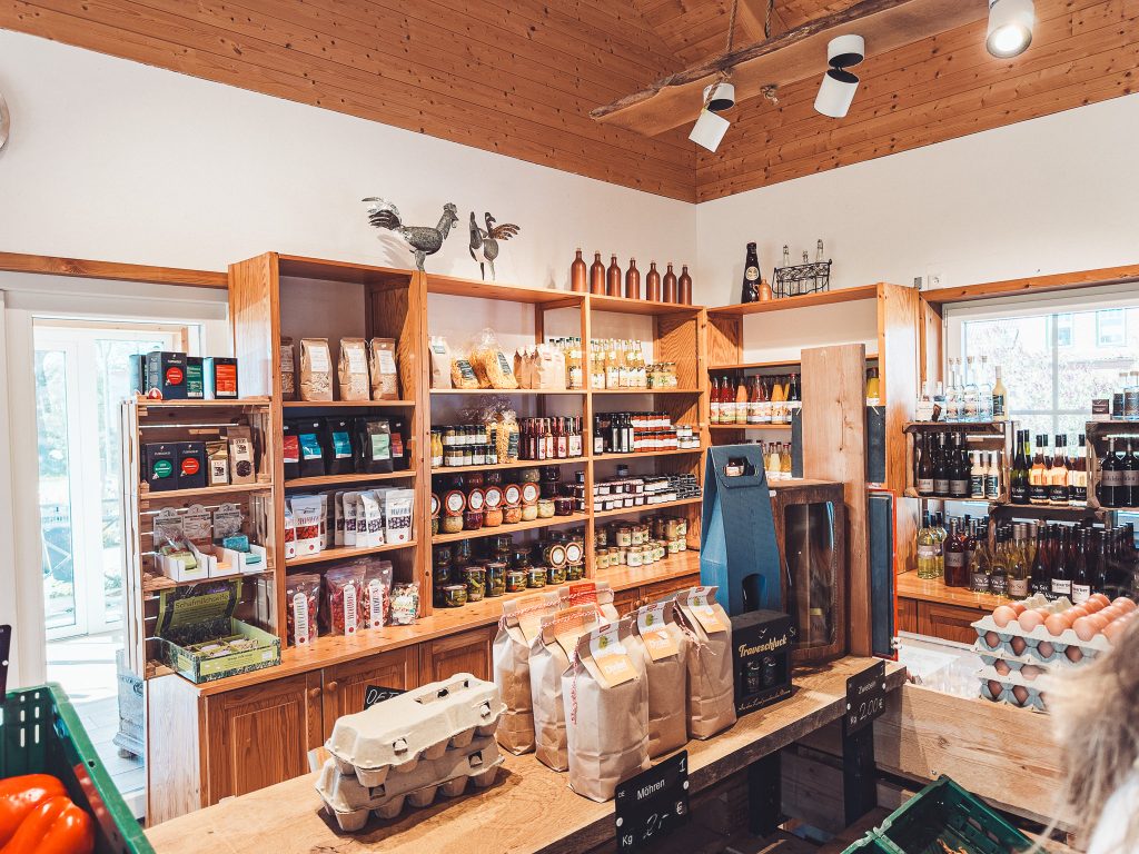 Interior of a shop with wooden shelves filled with jars, bags and bottles, eggs on the counter, and a warm wooden ceiling behind them.