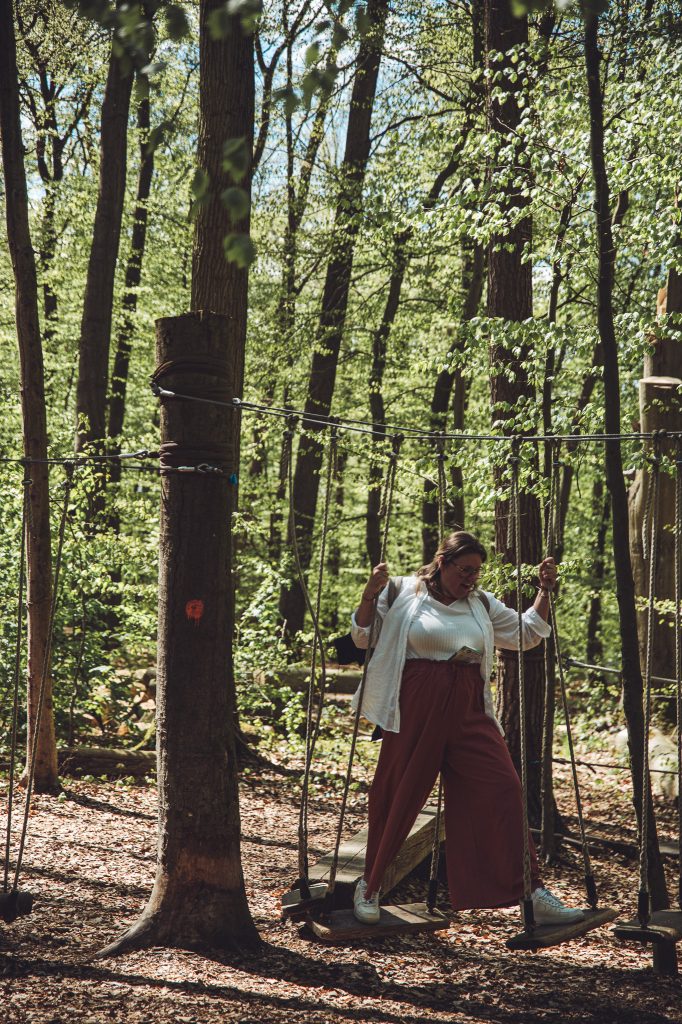Frau balanciert im Niedrigseilgarten des Otterzentrums Hankensbüttel zwischen Seilen und Holzstufen im Wald.