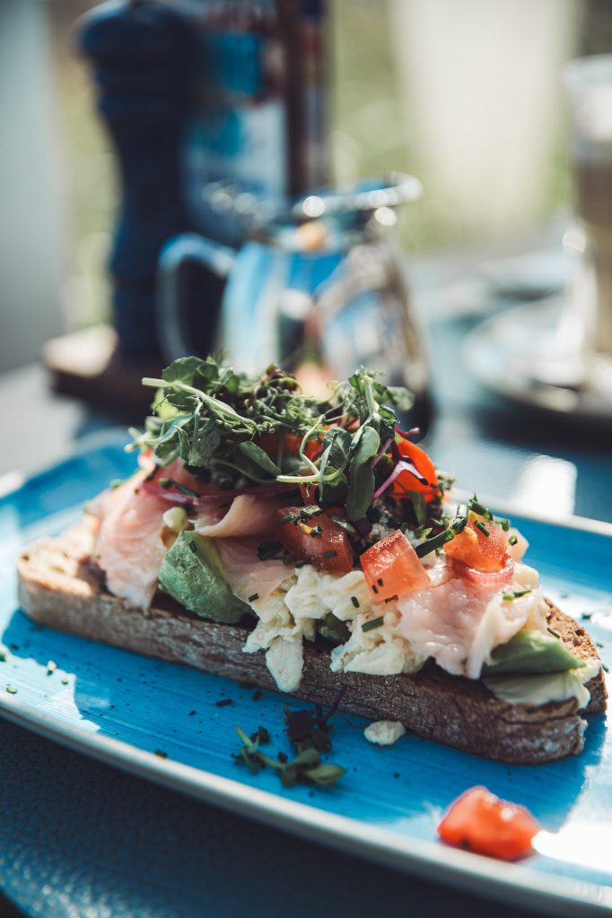 Belegtes Brot mit Fisch, Avocado, Rührei, Tomaten und Kräutern auf blauem Teller