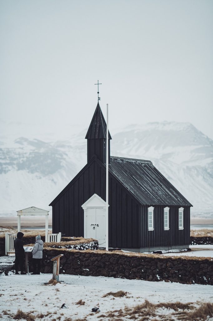 Schwarze Kirche Búðakirkja mit weißer Tür vor verschneiten Bergen auf Snæfellsnes
