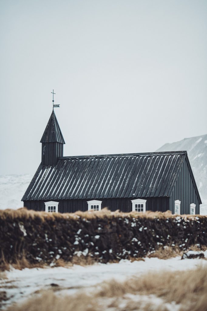 Seitlicher Blick auf die schwarze Kirche Búðakirkja mit weißen Fenstern und Schneeresten