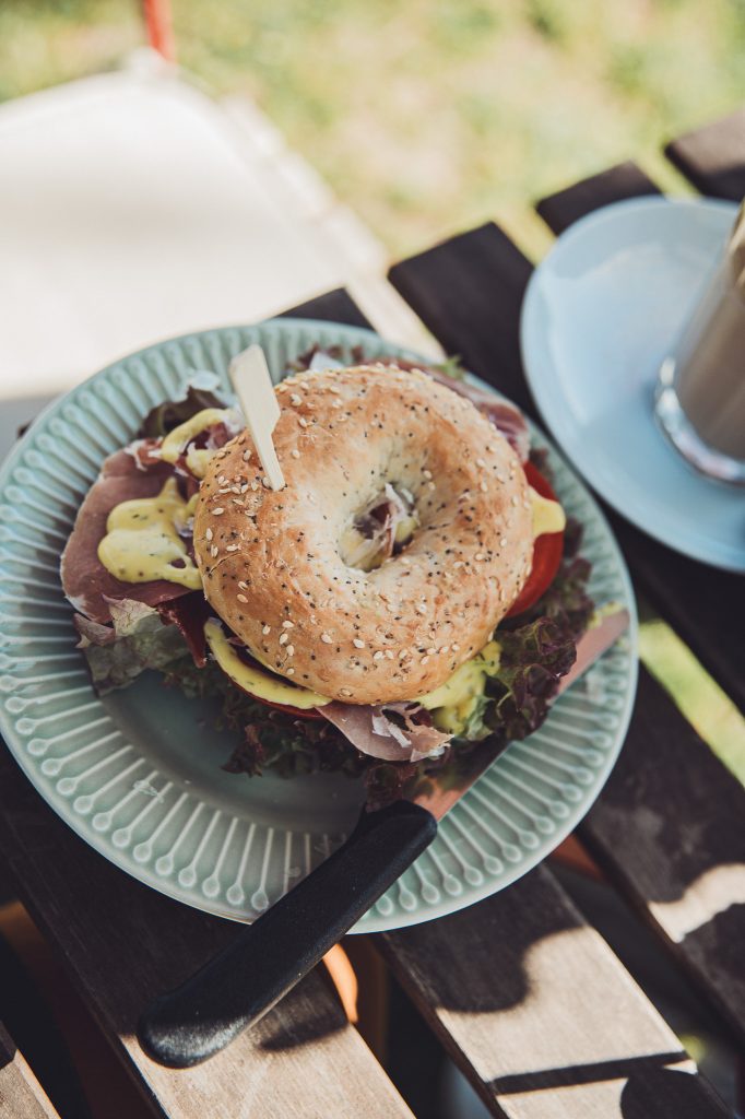 Nahaufnahme eines Bagels mit Schinken, Salat, Tomate und Sauce auf einem Teller im Hofcafé Blümels