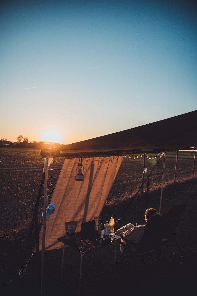 Camper Stellplatz bei Blümels Hof mit Markise, Tisch, Stuhl und Sonnenuntergang über dem Feld