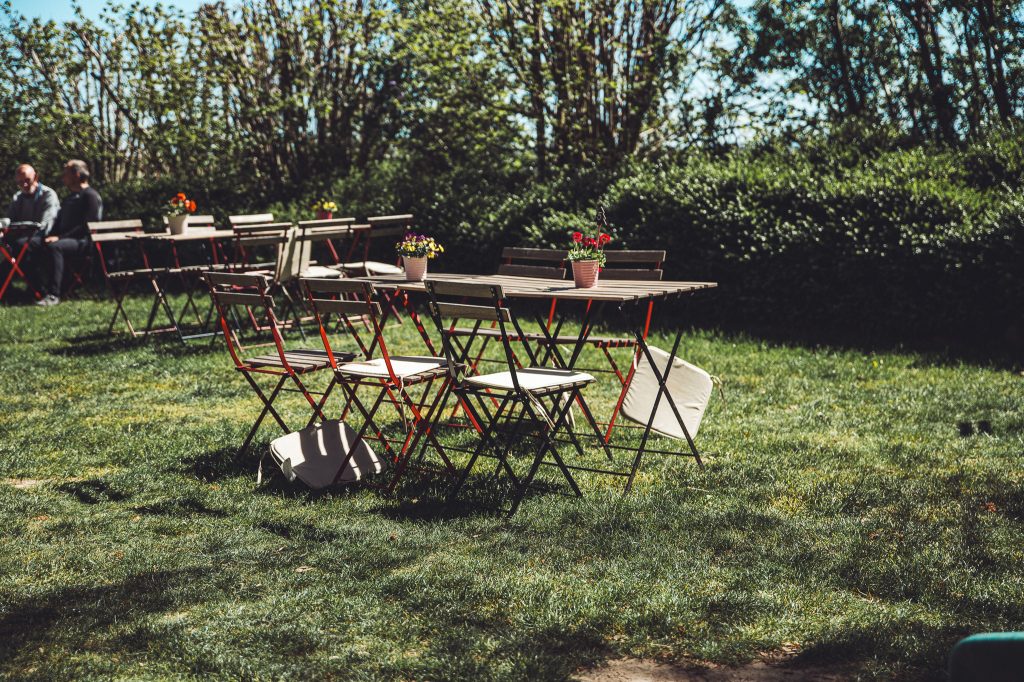 Tische und Stühle im Garten vom Hofcafé bei Blümels Hof mit Sonne und grüner Hecke
