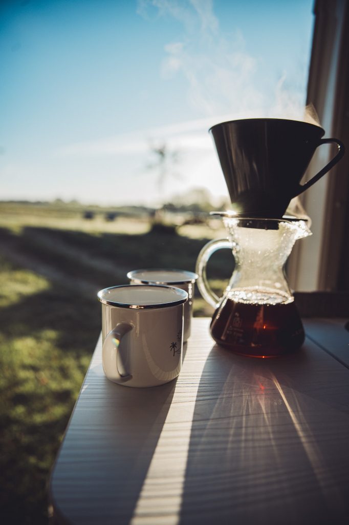 Filterkaffee und Emailletassen im Camper mit Blick aufs Feld