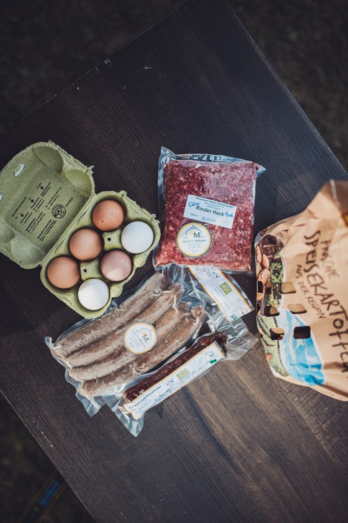 Hofladen Einkauf mit Eiern, Würstchen, Hackfleisch, Salami und Kartoffeln auf einem Campingtisch