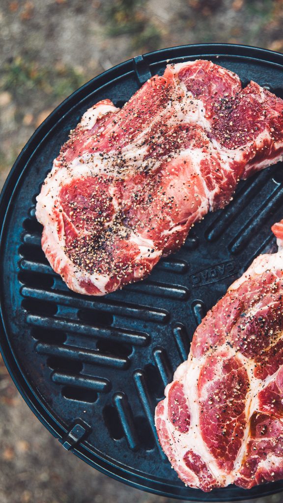 Gewürzte Steaks auf einem Grill während der Landvergnügen Camperreise