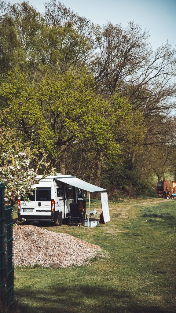 Weißer Camper mit ausgefahrener Markise auf dem Stellplatz bei Krügers Hof am Waldrand.