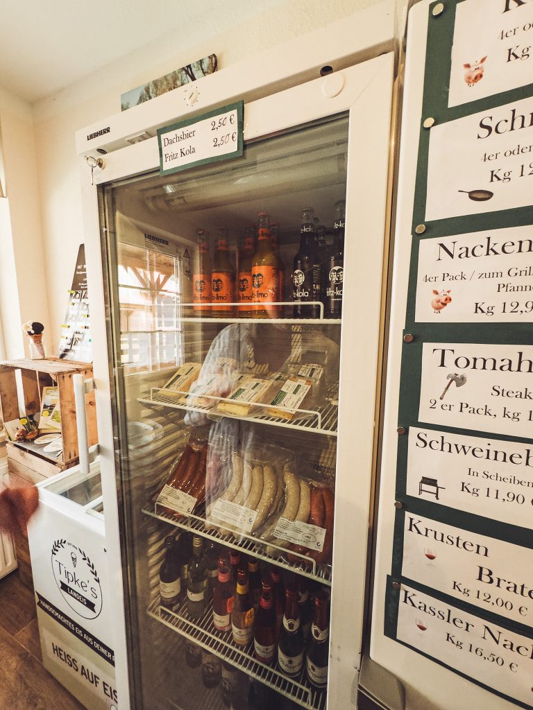Kühlschrank im Hofladen von Krügers Hof mit Fleisch, Würstchen, Getränken und Preisschildern daneben.
