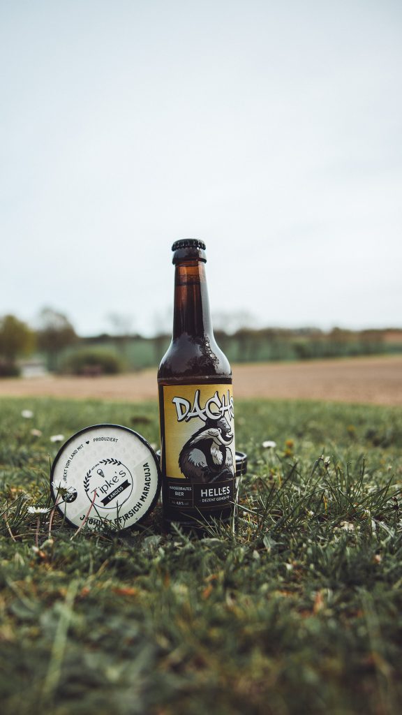 Flasche Bier und Eisbecher aus dem Hofladen von Krügers Hof auf einer Wiese vor einem Feld.