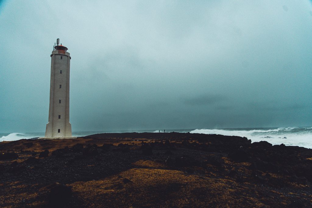 Leuchtturm von Malarrif mit dunklem Lavafeld und hohen Wellen an der Küste von Snæfellsnes