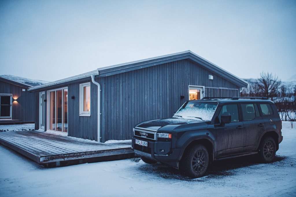 Blue wooden house with large glass doors, snow on the ground, and a dark Toyota SUV parked in front.