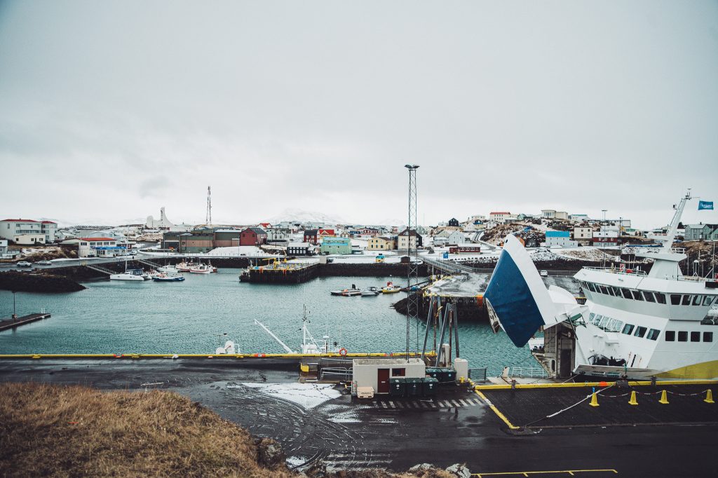 Harbor scene with colorful houses along the shoreline and docked boats under a cloudy sky.