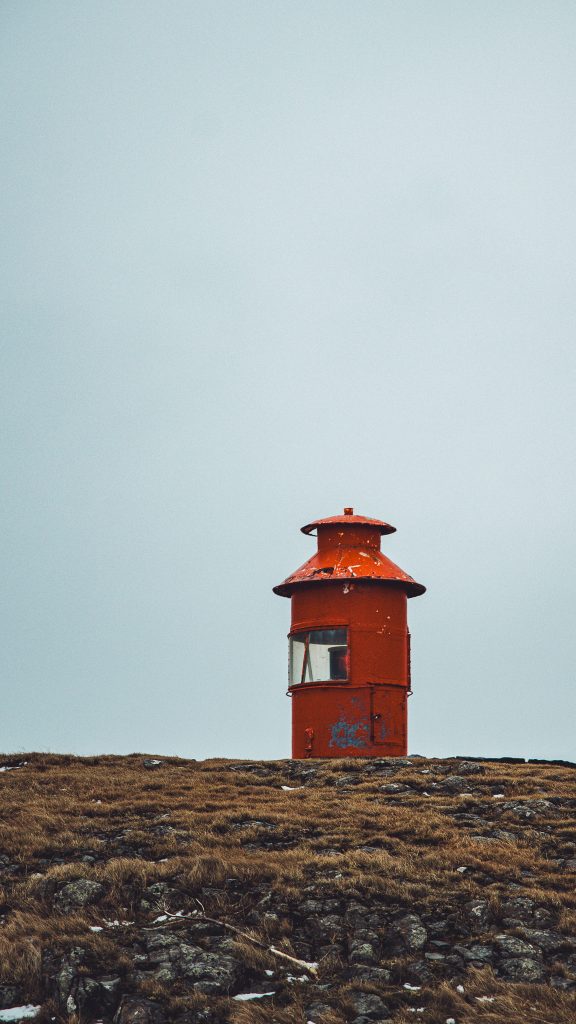 Roter Leuchtturm Súgandiseyjarviti auf einer grasigen Anhöhe in Stykkishólmur auf Snæfellsnes